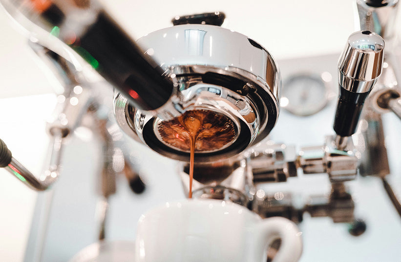 An upward view of espresso extracting from a naked portafilter on a polished chrome group head