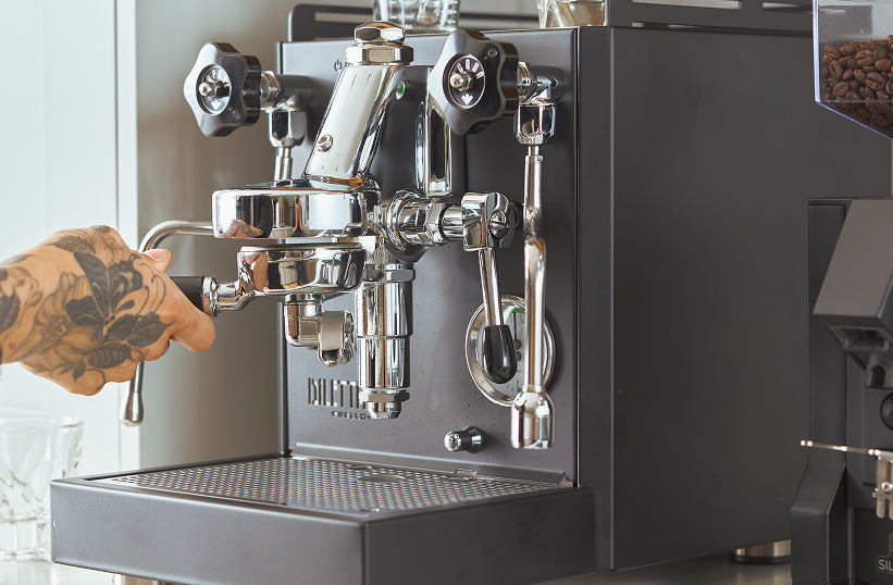 A tattooed hand locking a portafilter into a prosumer espresso machine group head