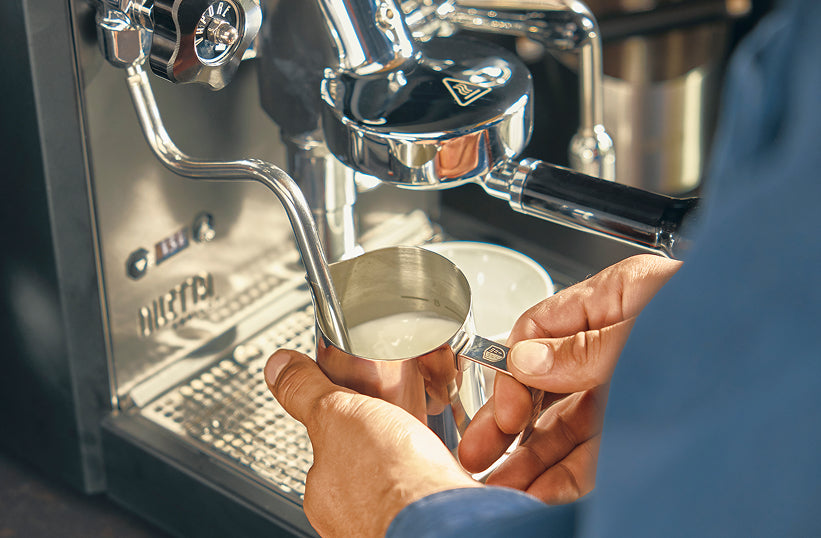 Hands holding a milk pitcher under the steam wand of a Bezzera espresso machine