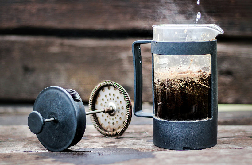 A disassembled French press plunger next to a carafe of coffee with steam rising