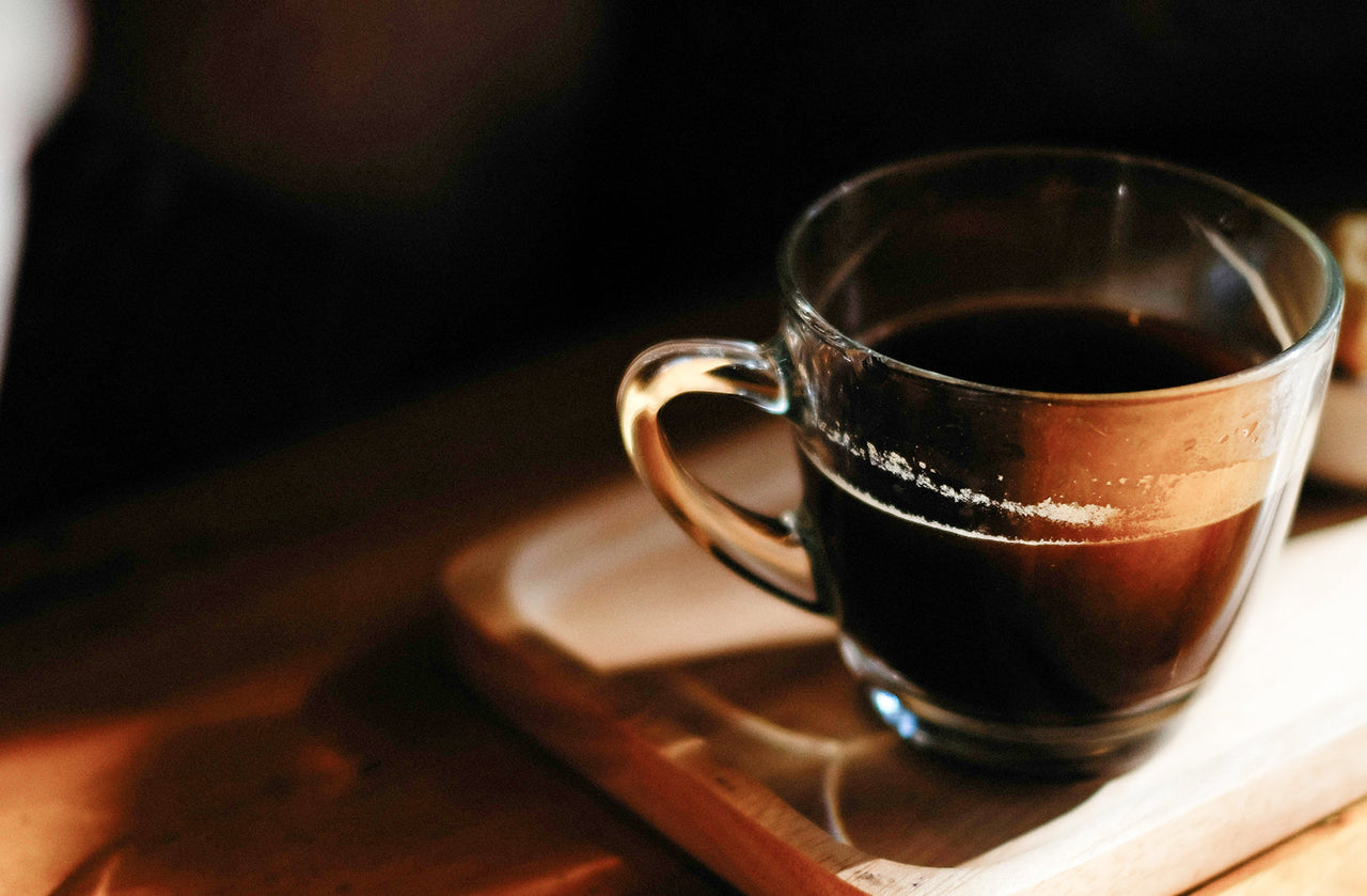 Glass cup of dark decaf espresso with crema on a wooden tray