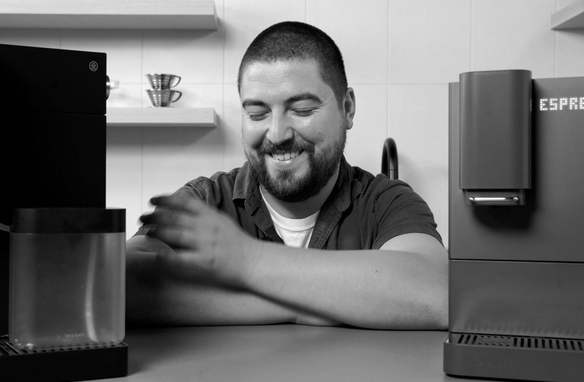 SCG crew member smiling between two Terra Kaffe superautomatic espresso machines - Seattle Coffee Gear