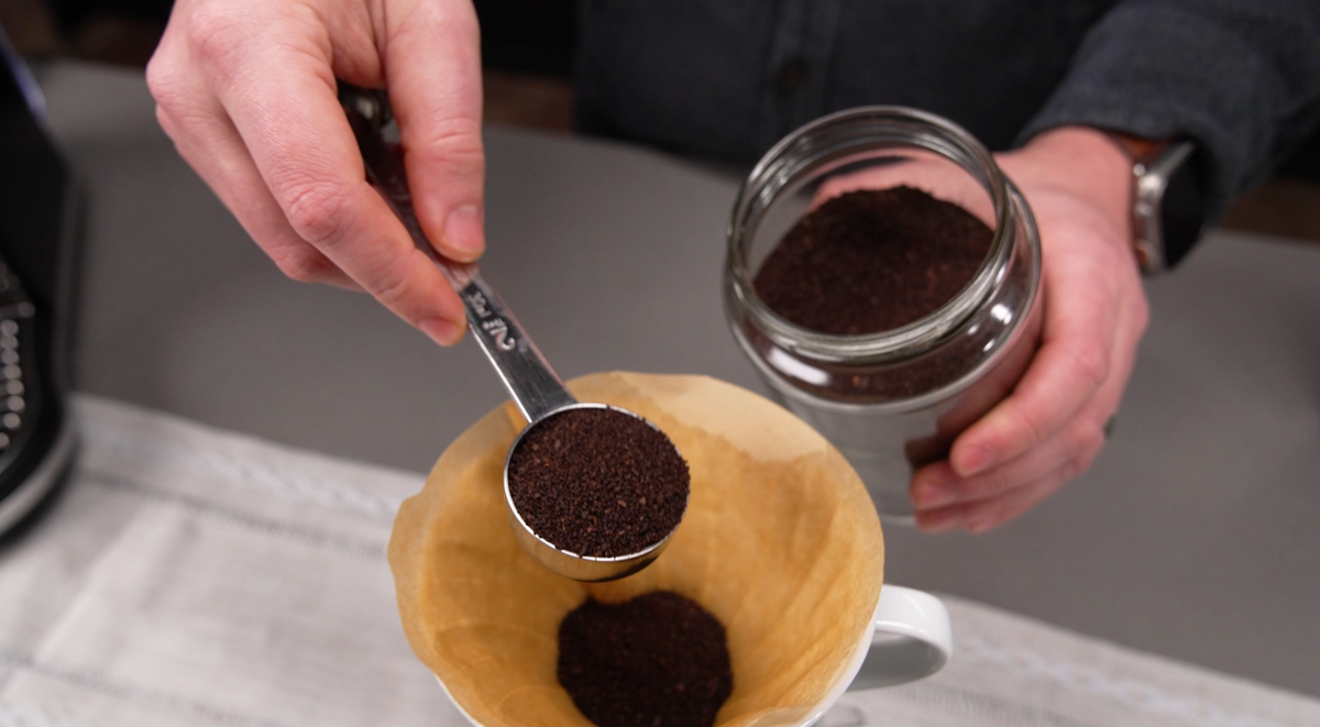 Scooping pre-ground coffee from a glass jar into a paper filter in a pour over dripper - Seattle Coffee Gear
