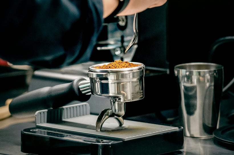 A barista distributing ground coffee in a portafilter basket with a WDT tool