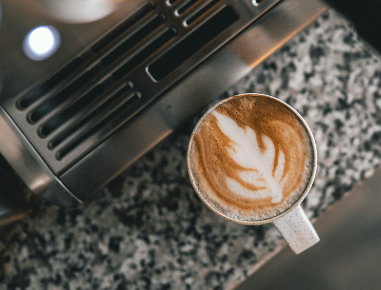 A cappuccino with latte art in a small ceramic cup sitting on a granite countertop next to an espresso machine