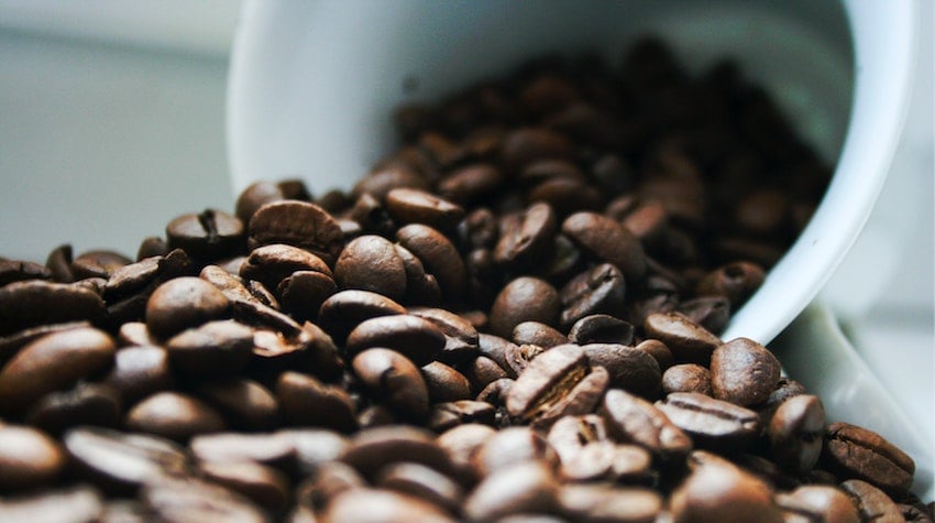 Coffee beans spilling out of a coffee cup onto a surface