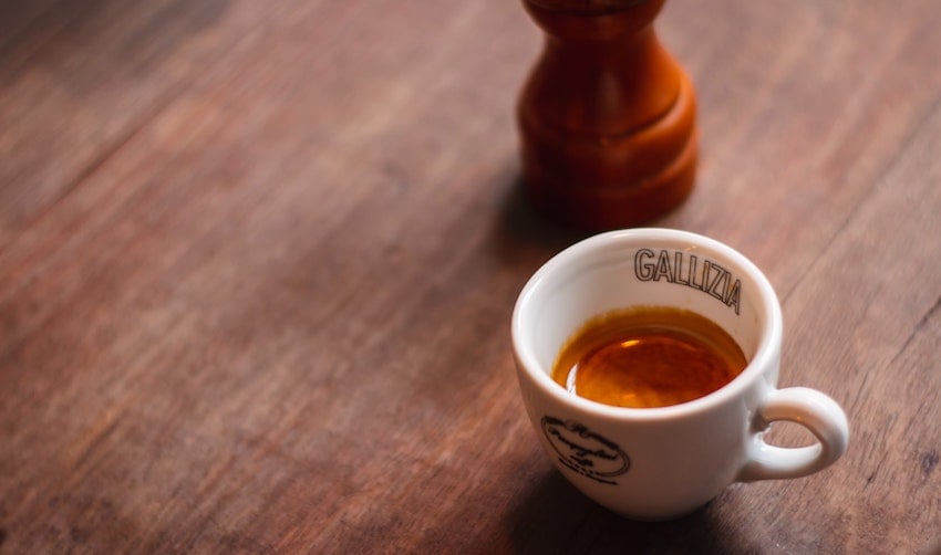 A cup of espresso on a table next to a coffee grinder